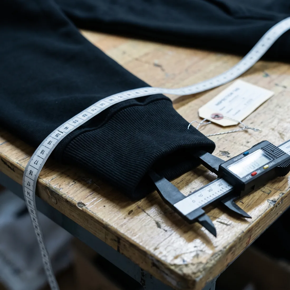 Digital caliper measuring the ribbed cuff of a black sweatshirt on a workbench